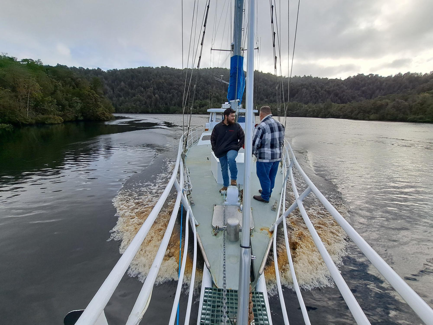 Two men standing on the bow of a motorised yacht sailing up the Gordon River Tasmania